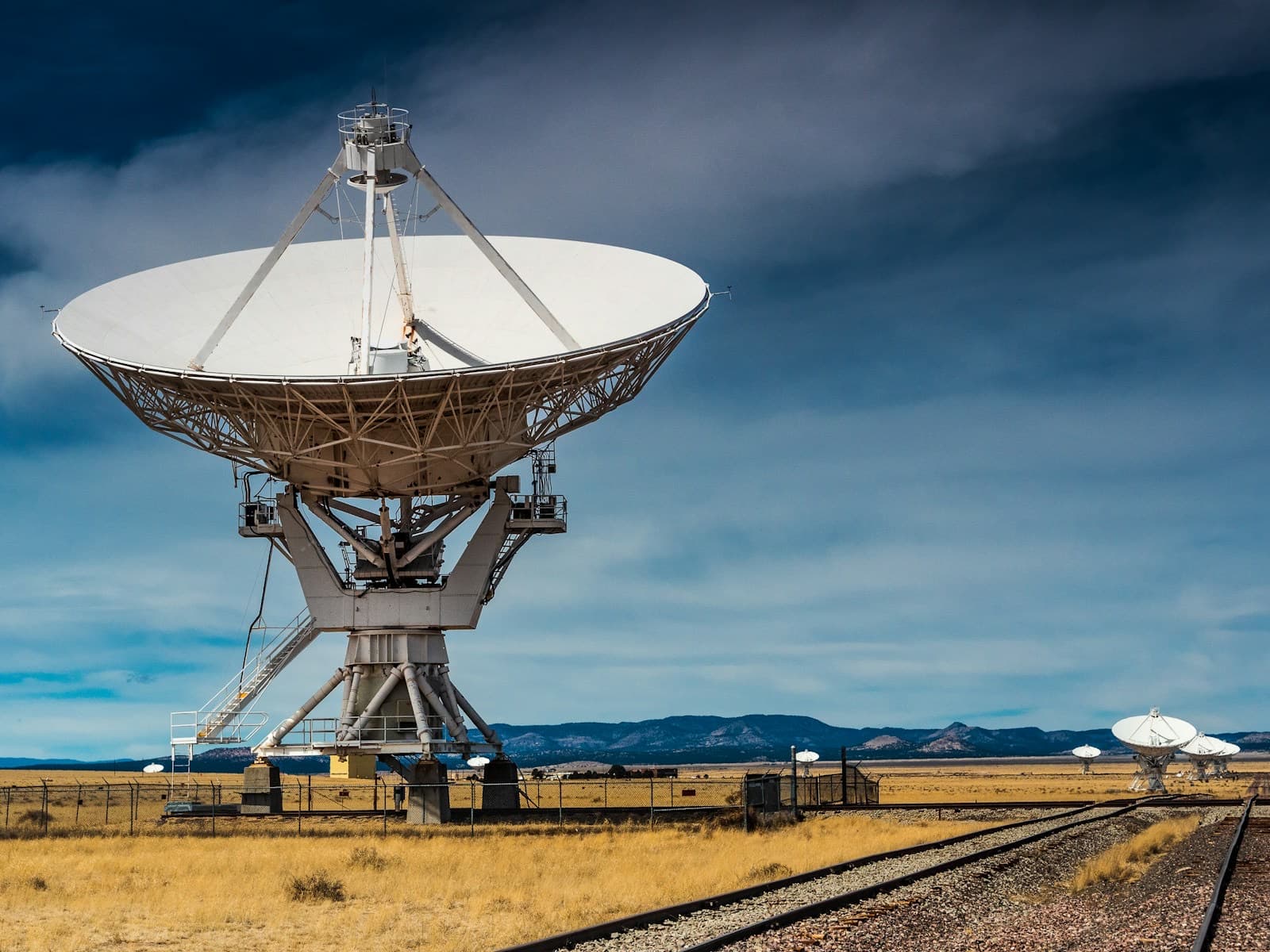 A row of large radio dishes on a plain under a stormy sky