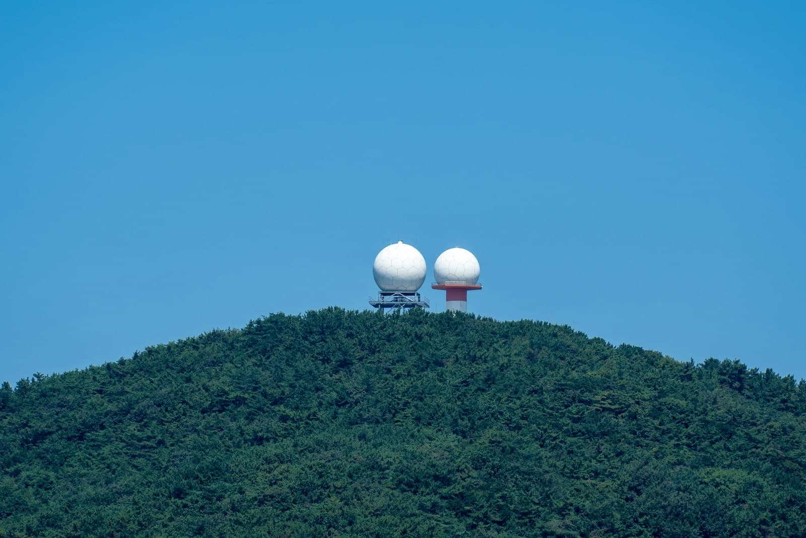 Two white radar domes on a forested hilltop under a clear sky